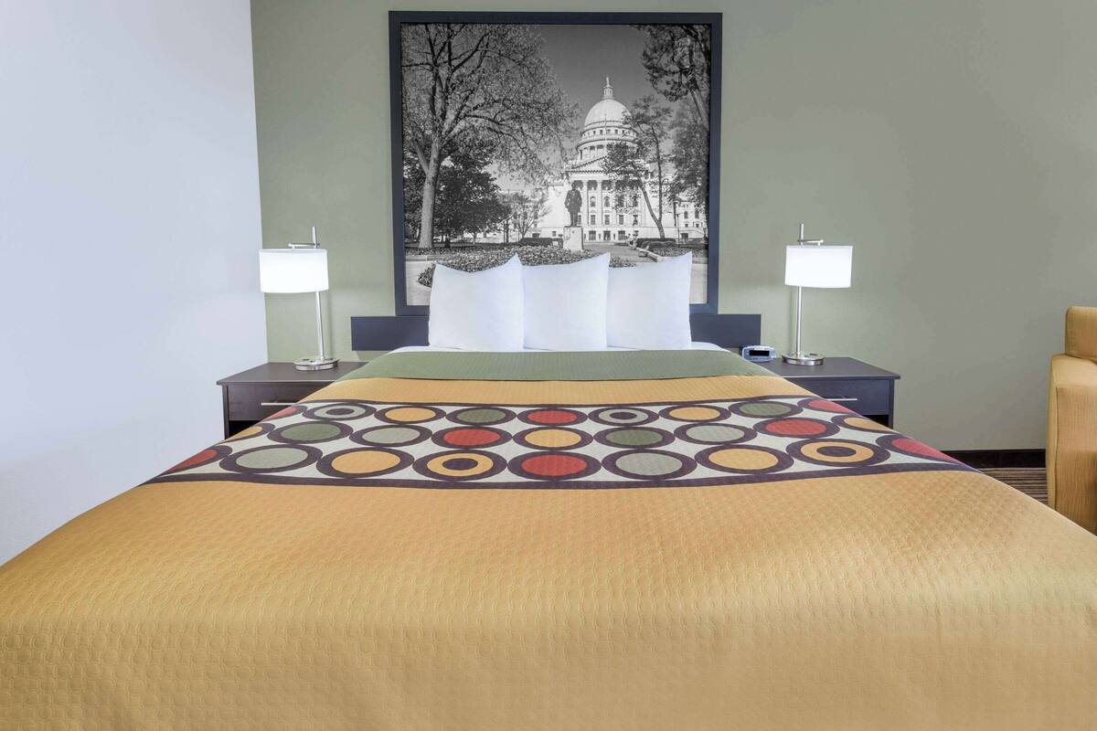 A hotel room with a bed, two bedside tables, and a large wall art of a building.