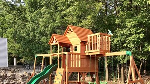Une structure de jeux en bois comprenant un toboggan, une échelle d’escalade et des balançoires.
