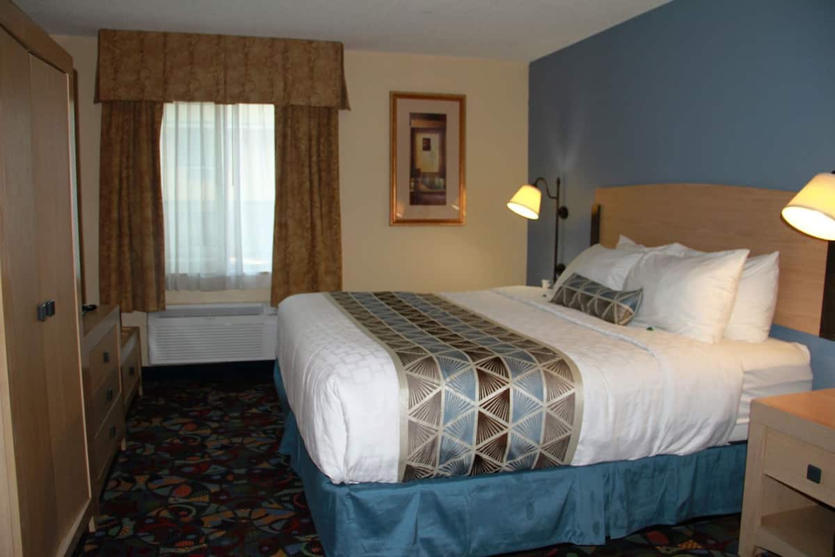 Une chambre d’hôtel avec un lit, une fenêtre avec des rideaux, une table de chevet et une lampe fixée au mur.