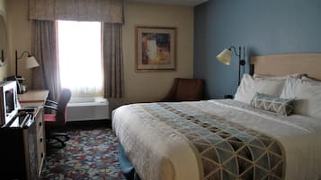 A hotel room with a bed, desk, chair, and a patterned carpet.
