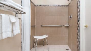 Un área de ducha con azulejos color beige, un asiento de ducha blanco, un perchero con toallas dobladas y una puerta con pomo dorado.