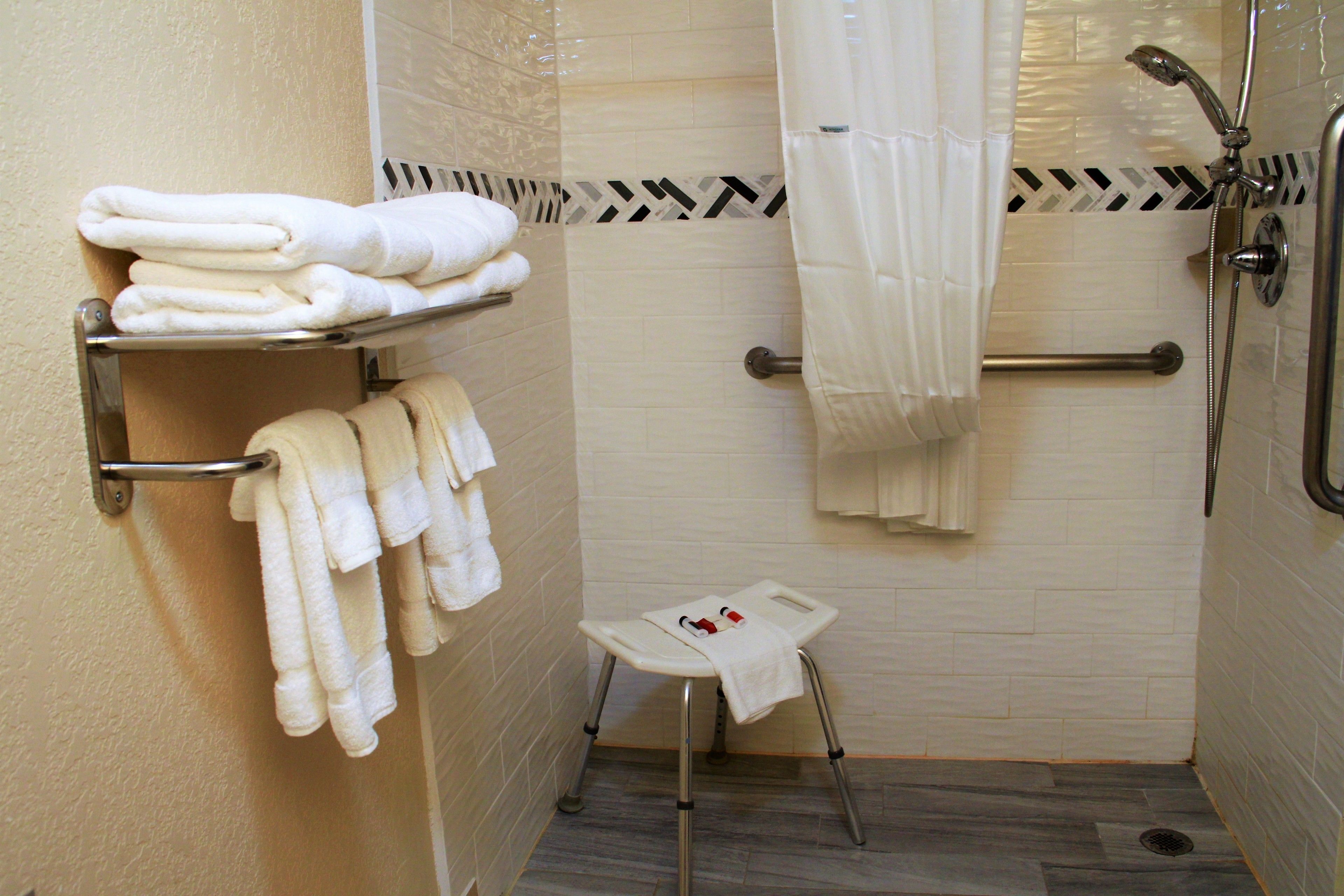 Un baño con ducha, un taburete pequeño y varias toallas en estantes.