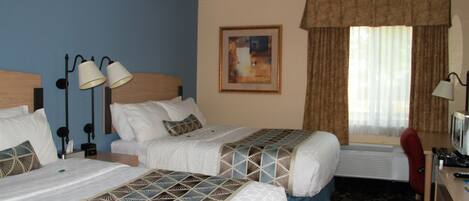 A hotel room with two beds, a ceiling fan, a desk with a computer, and a window with curtains.