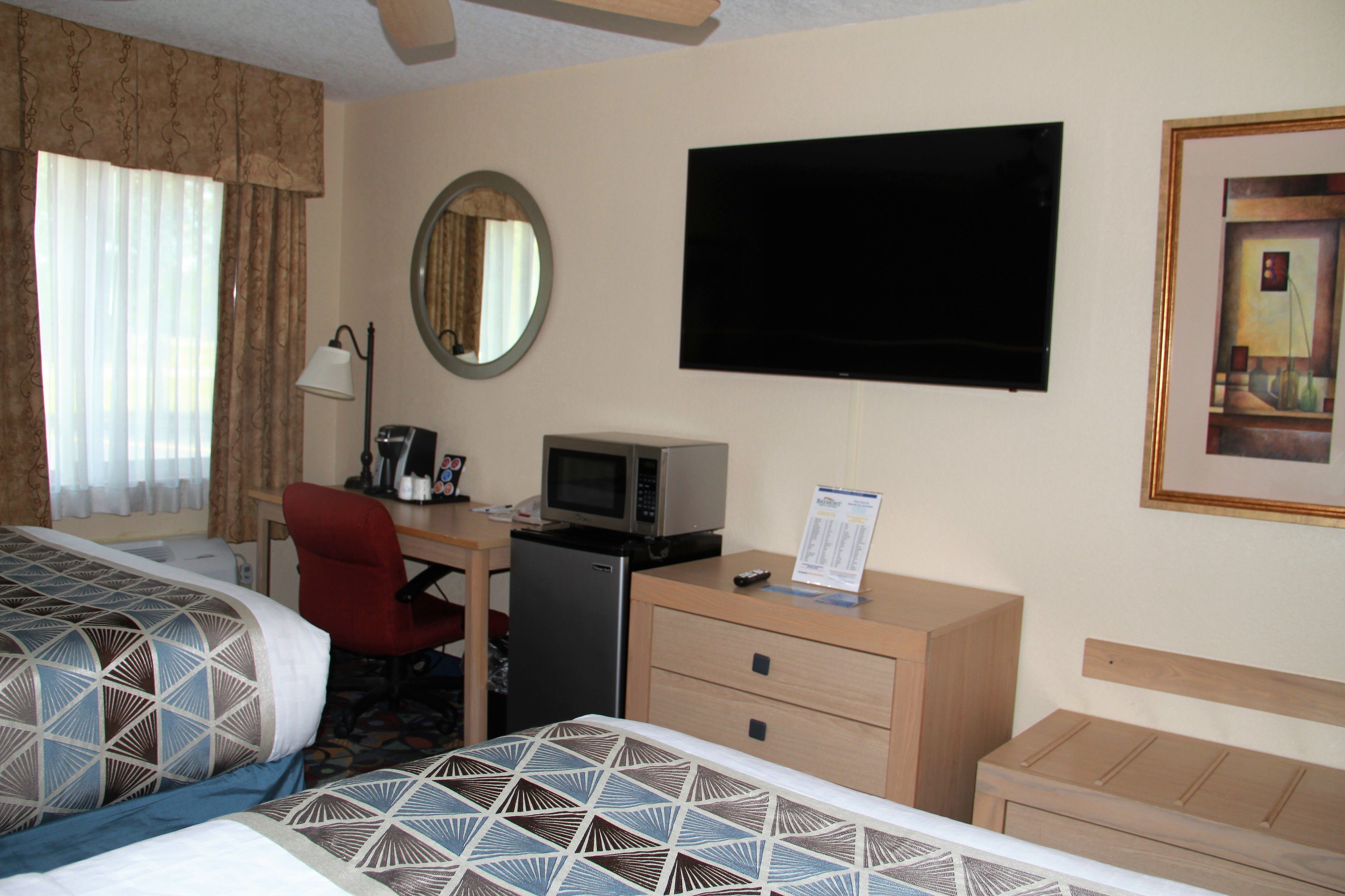 A hotel room with two beds, a desk with a microwave, a TV, a mirror, and a framed picture on the wall.