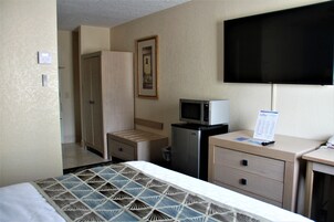 A hotel room with a bed, a desk, a television, a microwave, and a wardrobe.