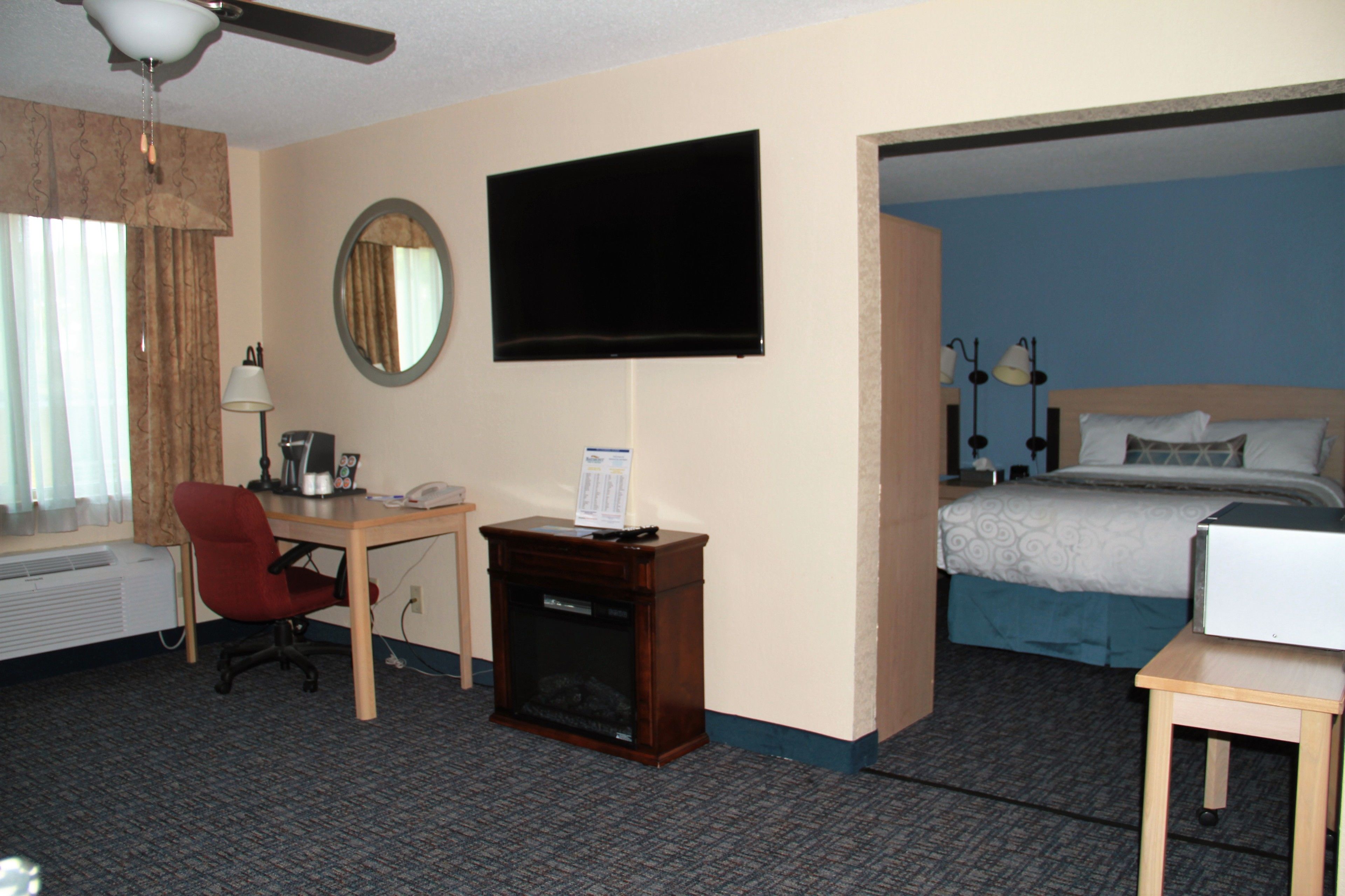 Habitación de hotel con cama, escritorio y silla, televisor montado en la pared y una mesita.
