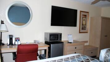 Una habitación de hotel con una cama, un escritorio con computadora, microondas, cafetera y televisor.
