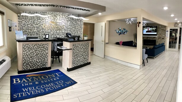 Un espace d'accueil avec une enseigne Baymont Inn & Suites, un comptoir de réception, un coin salon avec un canapé bleu et un écran de télévision.