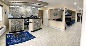 Un espace d'accueil avec une enseigne Baymont Inn & Suites, un comptoir de réception, un coin salon avec un canapé bleu et un écran de télévision.