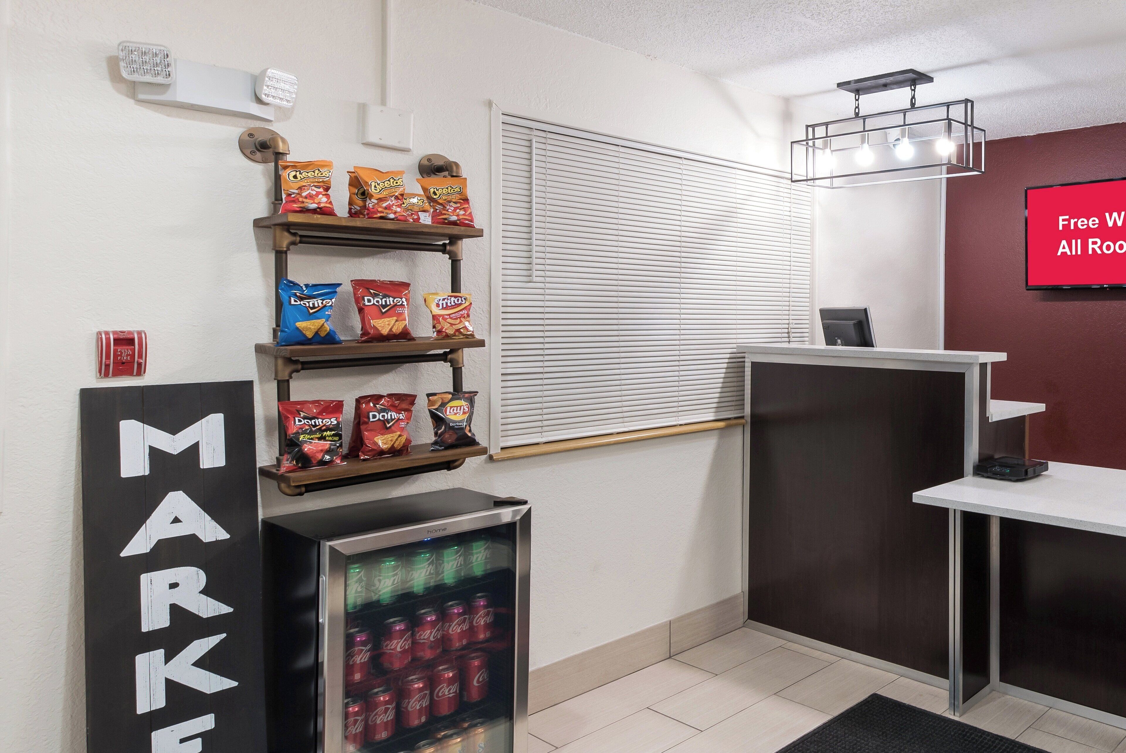 A kitchenette with a refrigerator stocked with beverages, shelves with snacks, and a 'MARKET' sign.