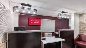 Ein Hotel-Rezeptionsbereich mit roter Wand, zwei Schreibtischen, einem roten Sofa und einem Schild, das kostenloses WLAN in allen Zimmern anzeigt.