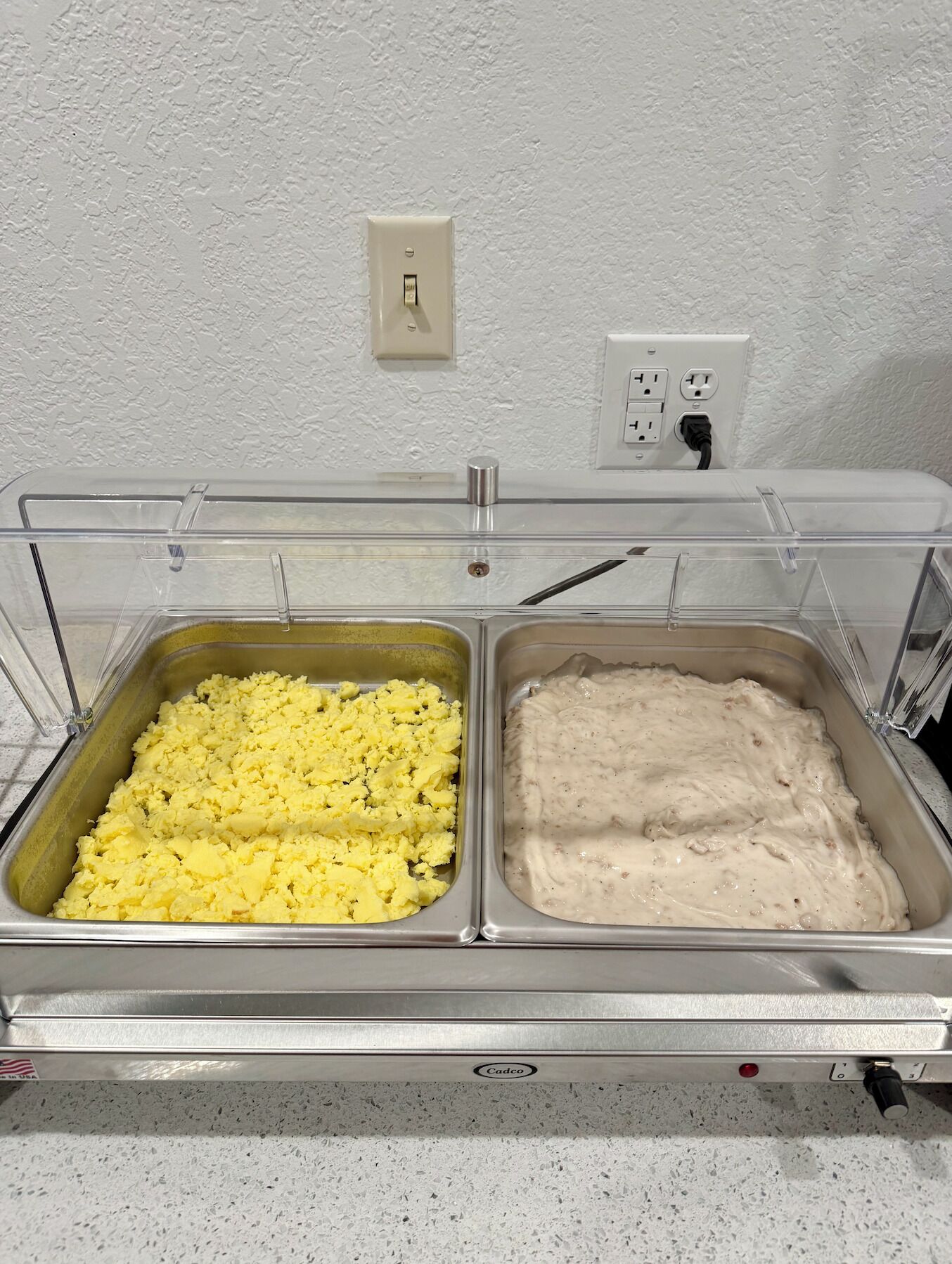 Un bufé con dos fuentes de comida: huevos revueltos y un plato cremoso.