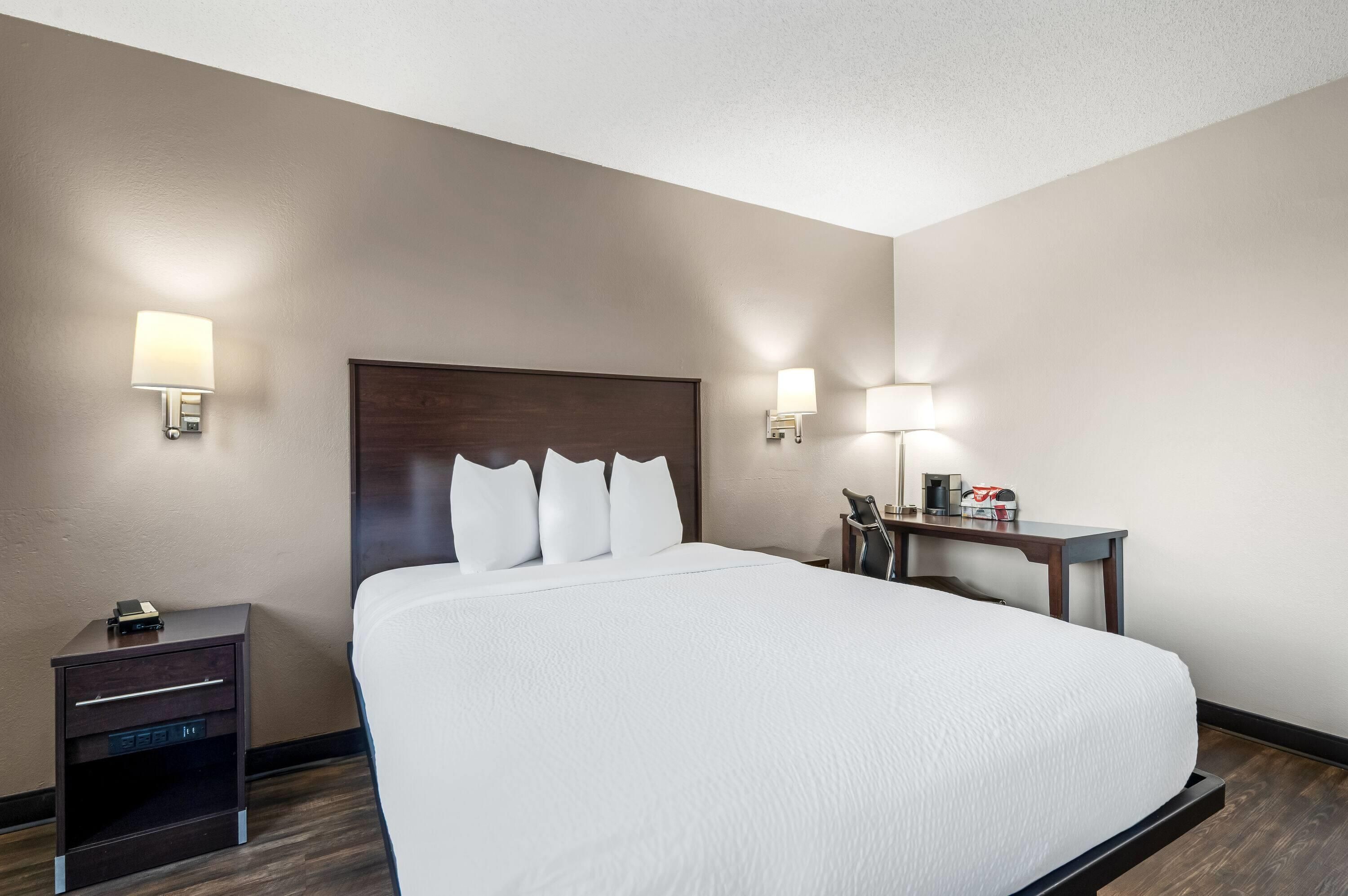 A hotel room with a large bed, bedside tables, a desk, and wall-mounted lamps.