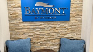 Schild für 'Baymont by Wyndham' vor einer Steinwand, mit zwei blau gepolsterten Sesseln und einem kleinen runden Tisch.
