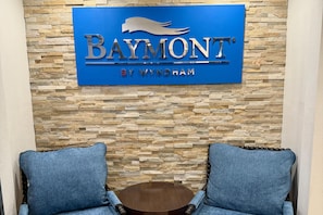 A sign for 'Baymont by Wyndham' with a stone wall backdrop and two blue upholstered chairs with a small round table in front. - Baymont by Wyndham Findlay (Findlay)