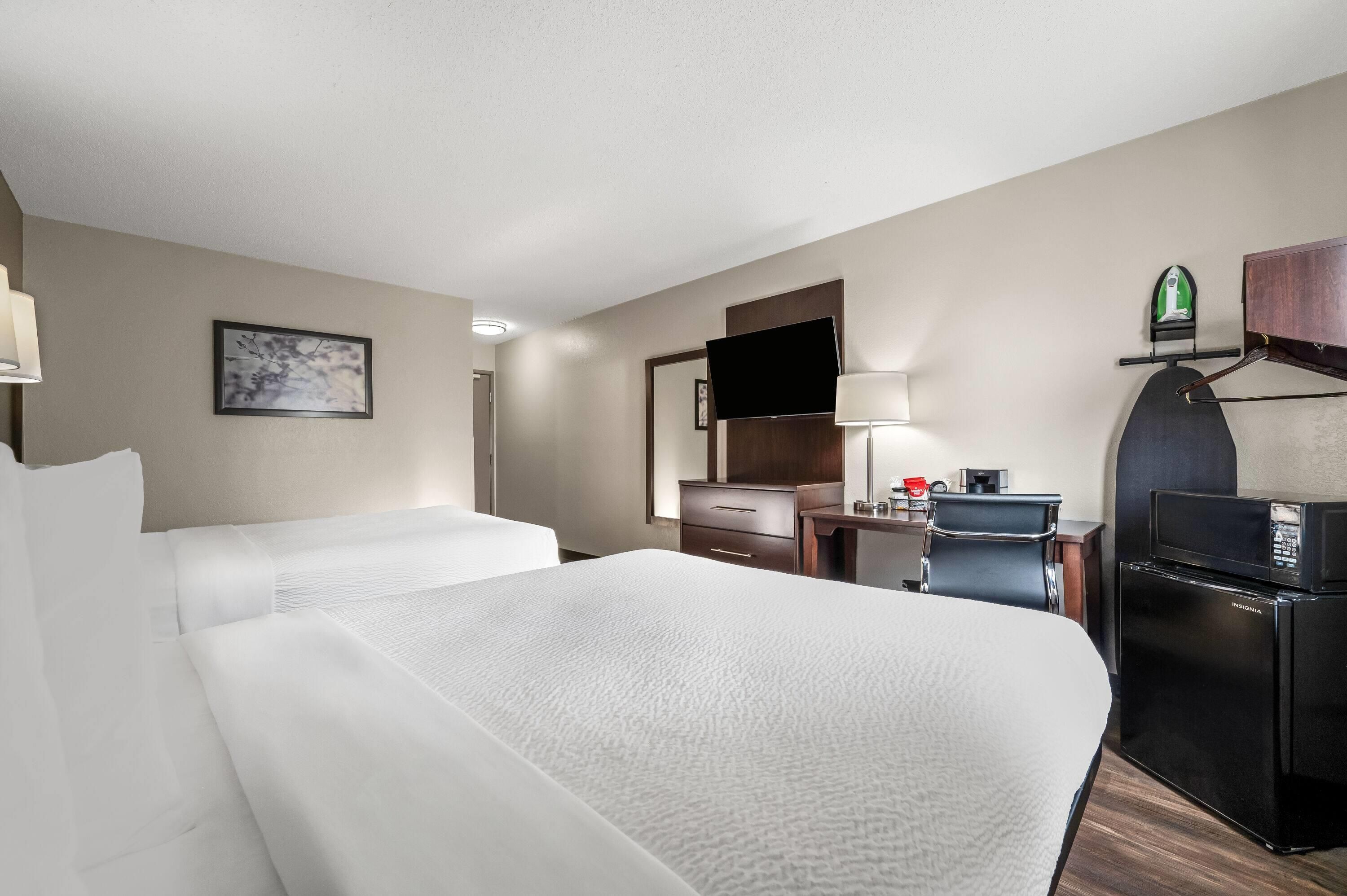 A hotel room with two beds, a desk with a computer, a refrigerator, a microwave, a TV, and a mirror.