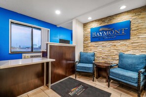A reception area with a blue wall, a Baymont sign, a reception desk, two armchairs, and a view through a window.