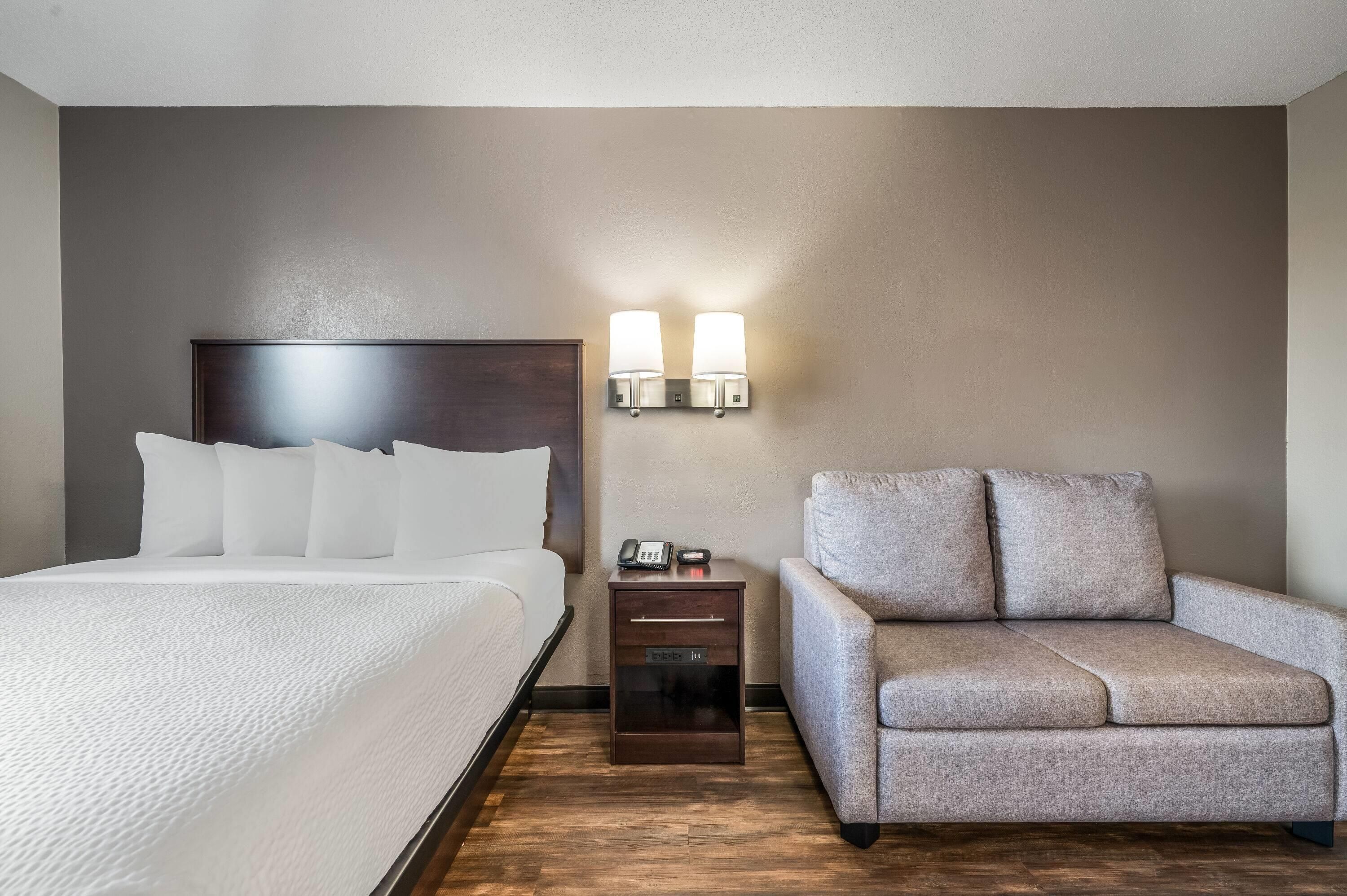 Una habitación de hotel con una cama, una mesita de noche con una lámpara y un sofá.