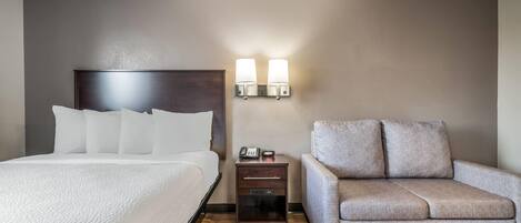 A hotel room with a bed, a nightstand with a lamp, and a sofa.