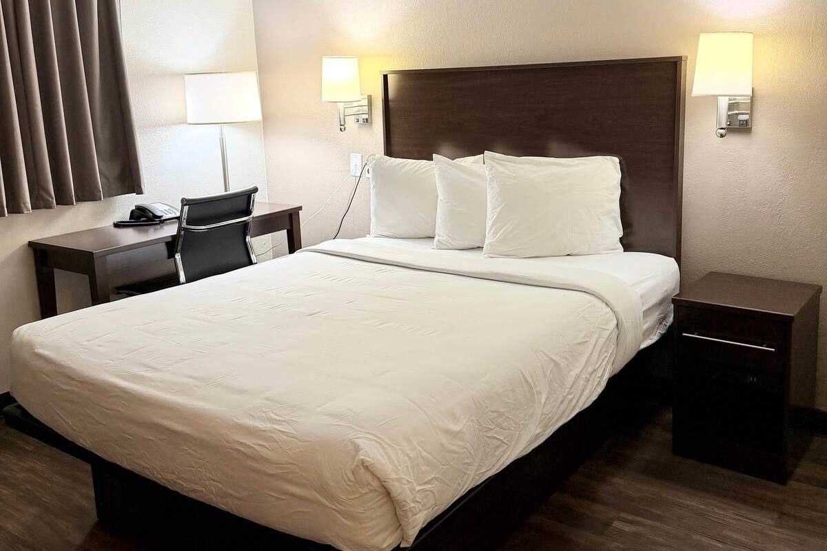 A hotel room with a large bed, bedside tables, a desk with a chair, and two wall-mounted lamps.