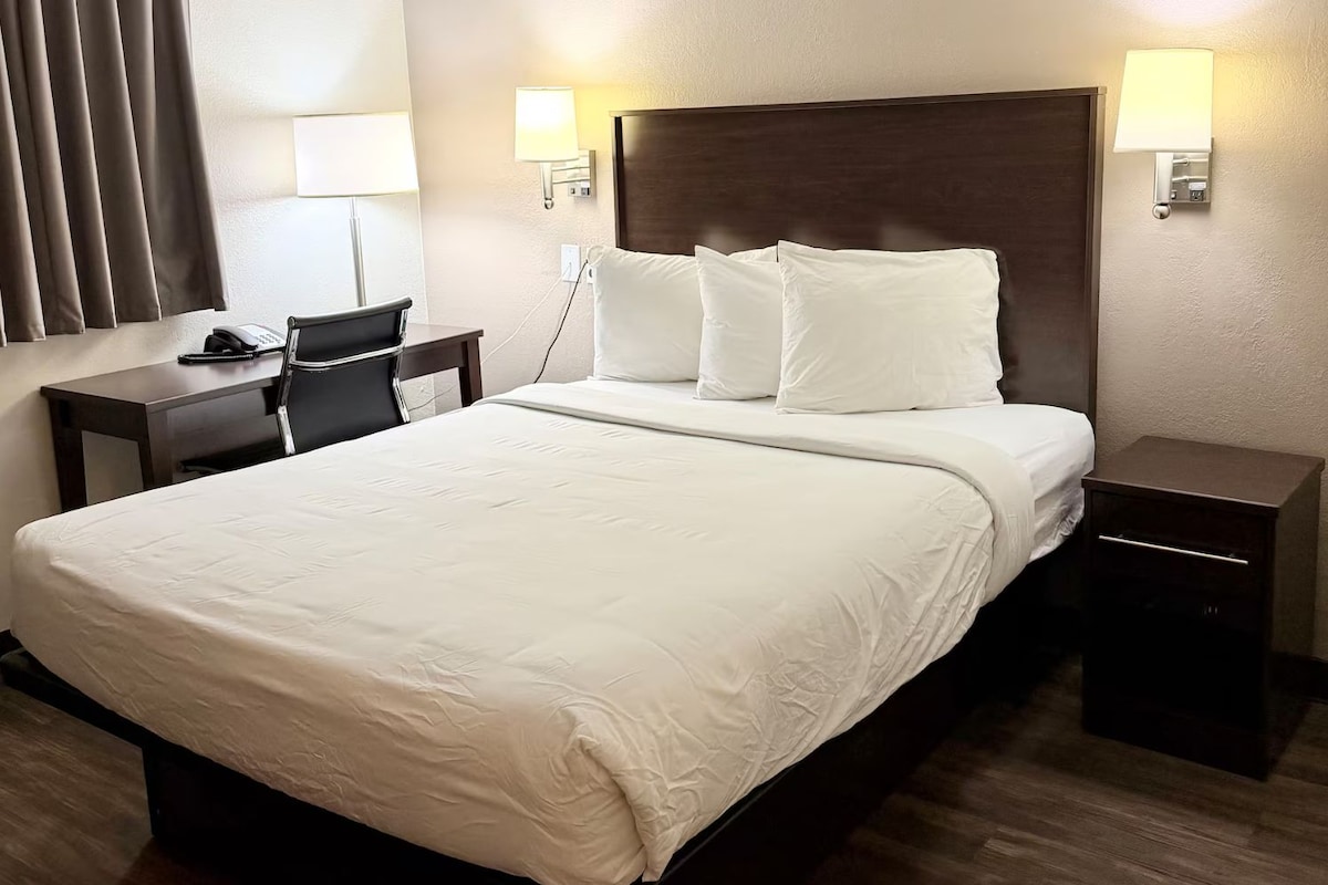 A hotel room with a large bed, a desk, a chair, and two bedside tables.