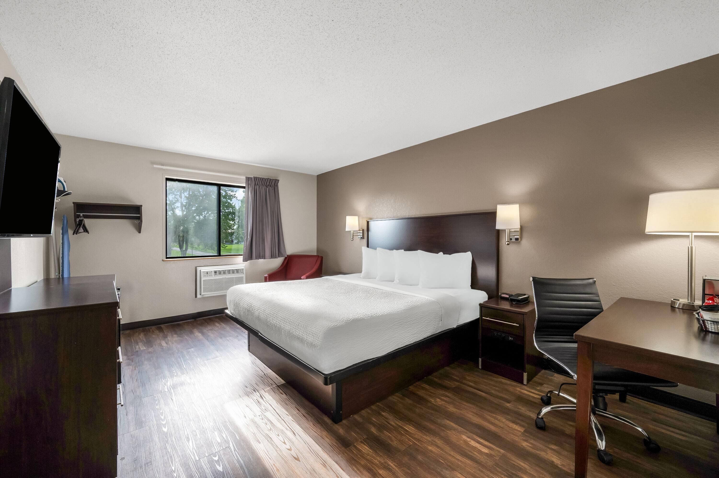 A hotel room with a bed, a desk, a chair, a TV, and a window with curtains.