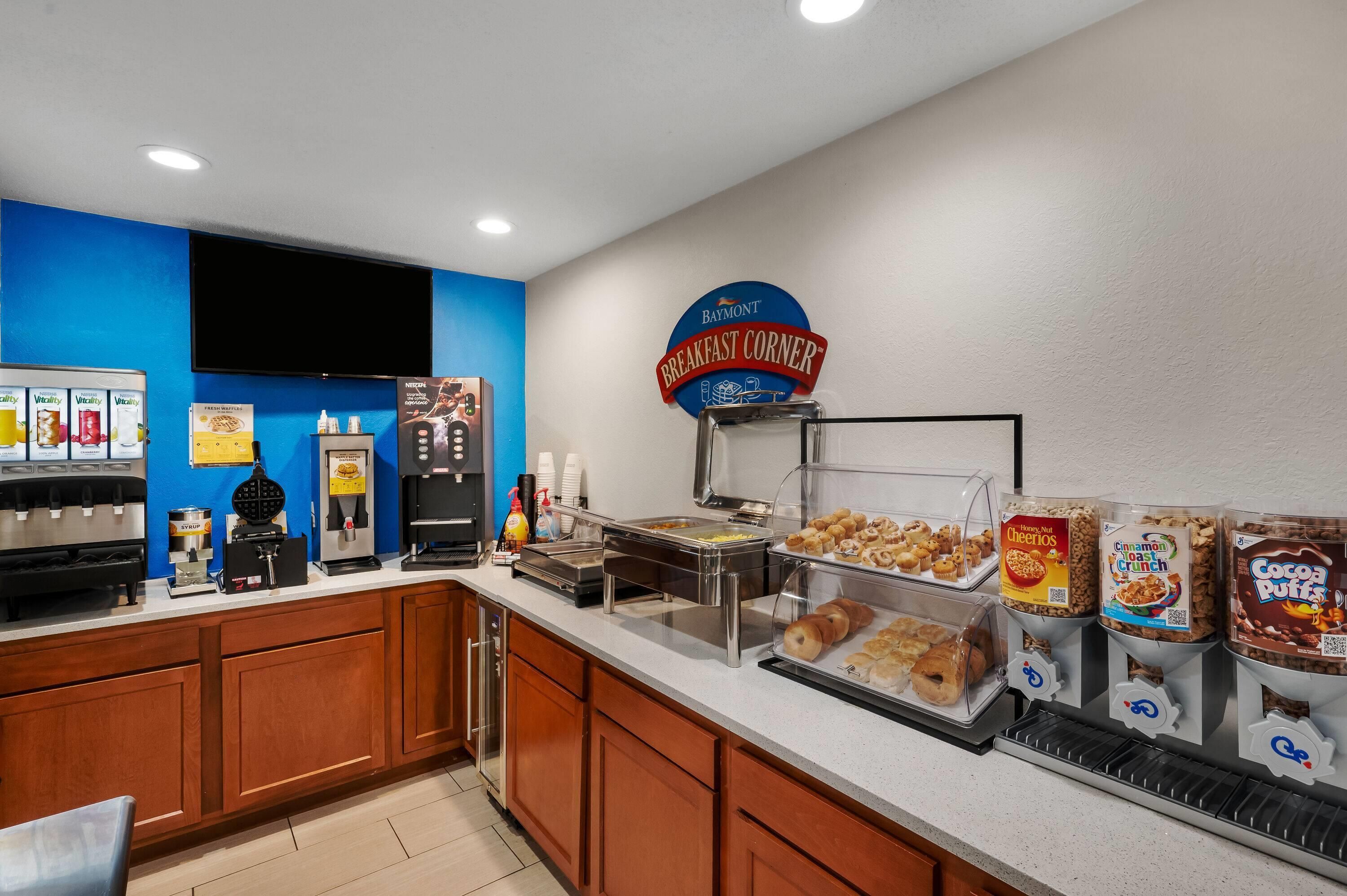 Espaço de buffet de café da manhã com diversas opções de comida, incluindo cereais, doces e uma estação de café.