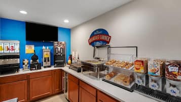 Espaço de buffet de café da manhã com diversas opções de comida, incluindo cereais, doces e uma estação de café.