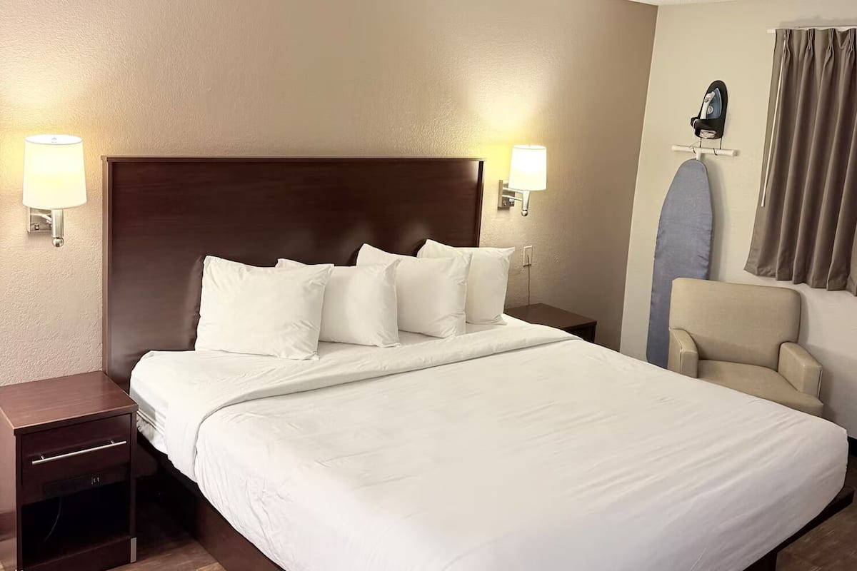 A hotel room with a large bed, two bedside tables, a chair, and a wall-mounted ironing board.