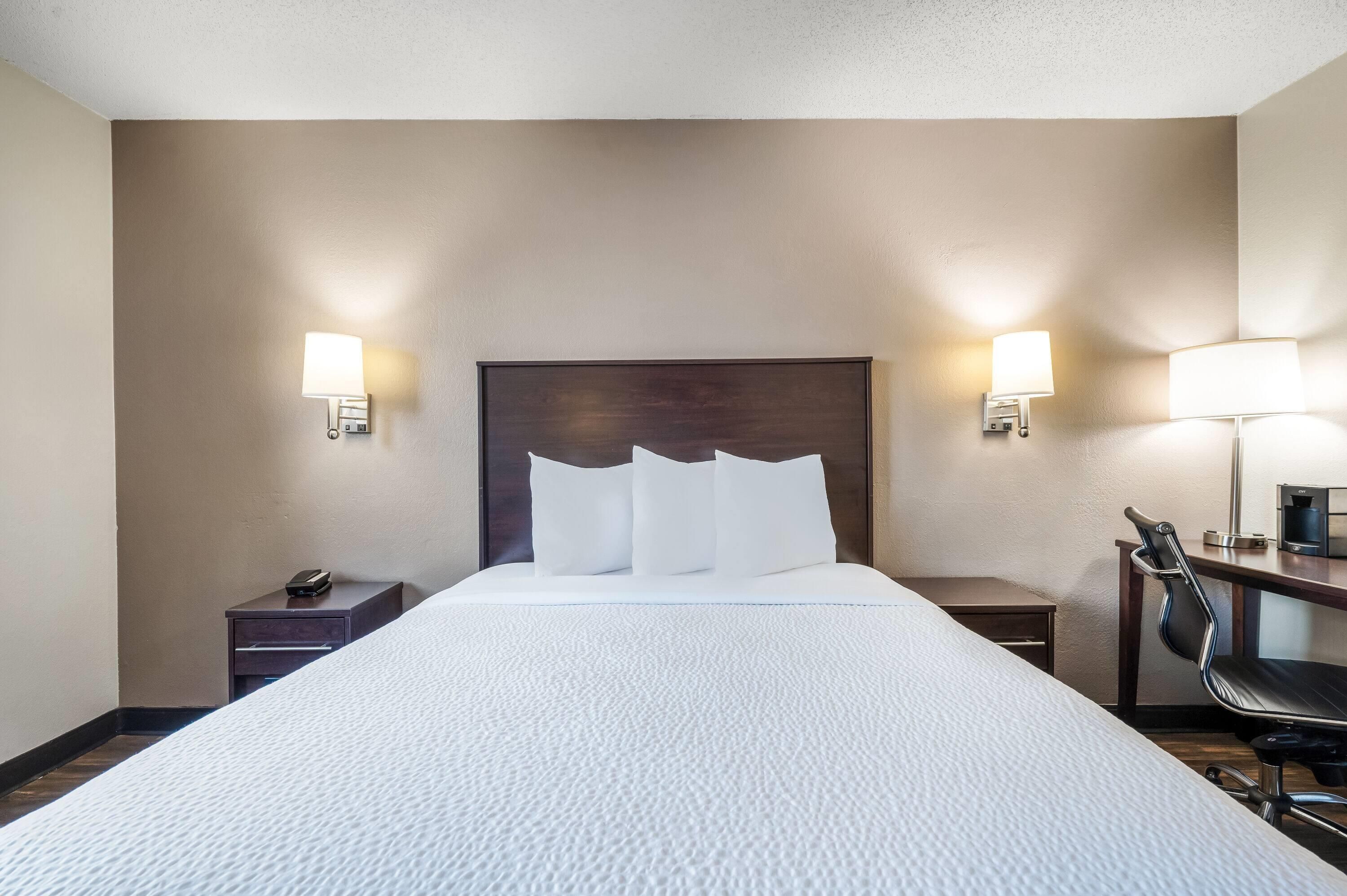 Quarto de hotel com uma cama grande, duas mesas de cabeceira, uma cadeira e duas luminárias na parede.