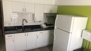 Eine Küche mit weißen Schränken, einer schwarzen Arbeitsplatte, einem Edelstahl-Spülbecken, einem weißen Kühlschrank und einer grünen Wand.