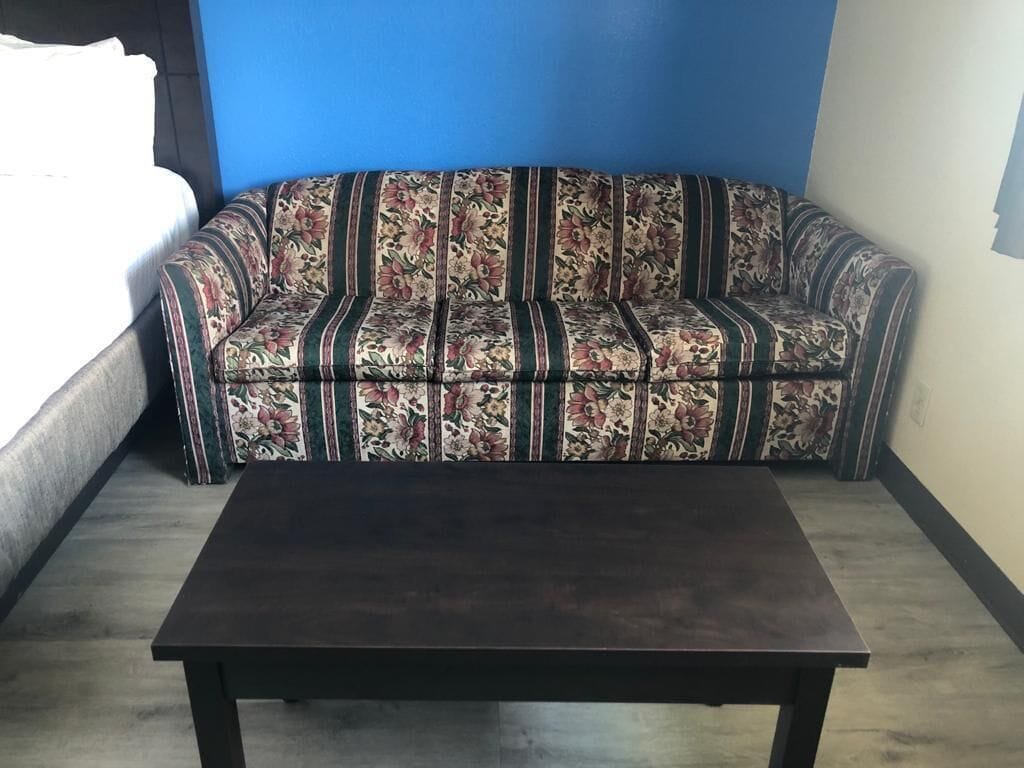 A room with a dark-colored sofa against a blue wall, a wooden coffee table, and a bed with white linens.