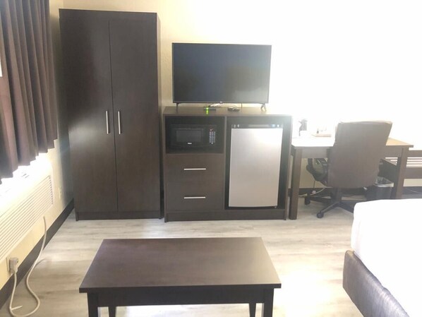 A hotel room with a bed, a desk with a computer, a television, a microwave, and a refrigerator.
