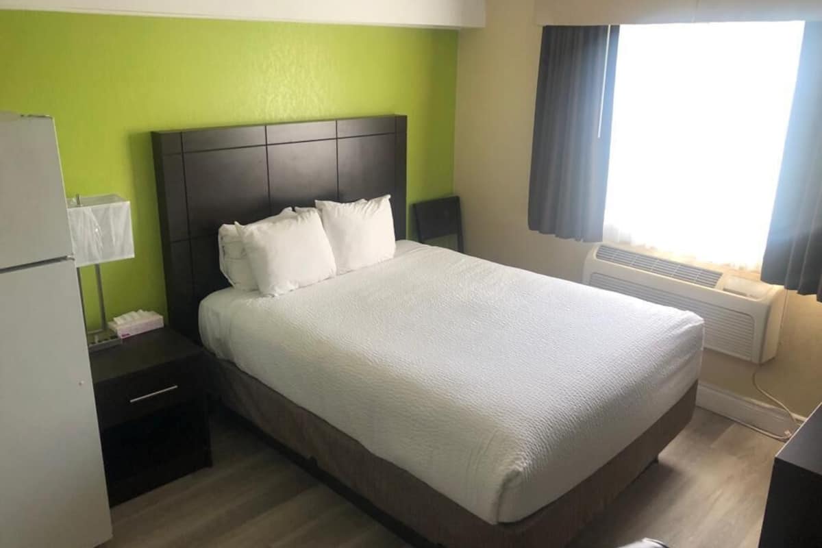 A hotel room with a large bed, a nightstand, a desk, and a window with curtains.