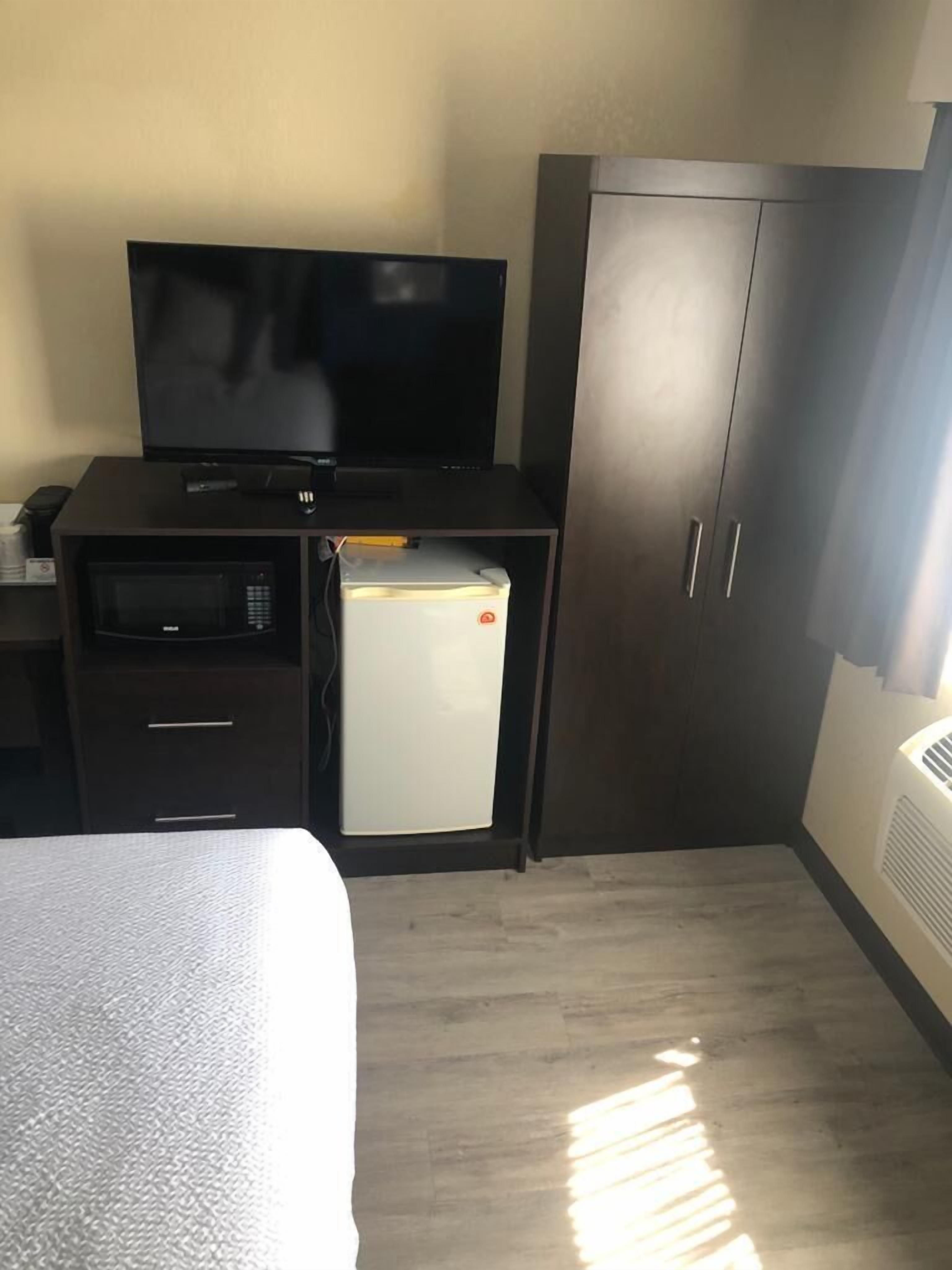 A compact hotel room with a bed, a small kitchenette, a television, and a wardrobe.