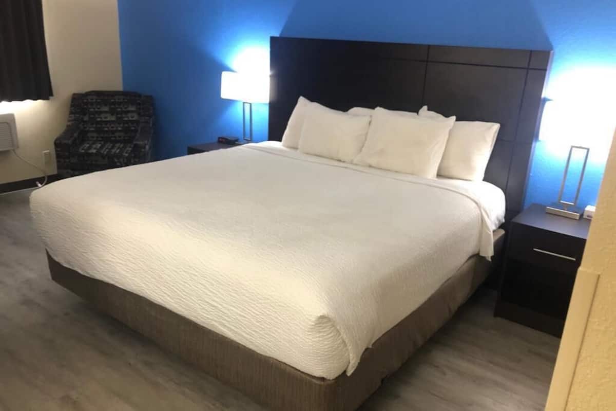 A large bed with a white comforter and pillows, a dark headboard, and a bedside table with a lamp.