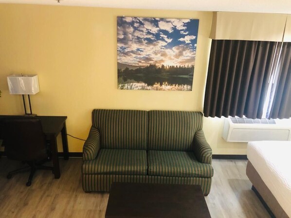A room with a striped sofa, a small table with a lamp, a bed, and a painting of a landscape on the wall.