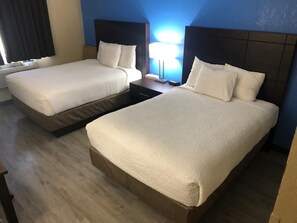 Habitación de hotel con dos camas, una mesita de noche, una lámpara y una ventana con cortinas.