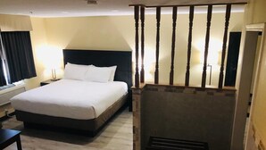 Ein Hotelzimmer mit einem großen Bett, einem Schreibtisch, einem Sessel, einem Kamin und einem Spiegel.