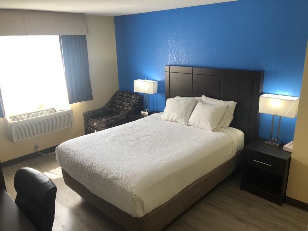A hotel room with a large bed, two bedside lamps, a chair, and a window with curtains.