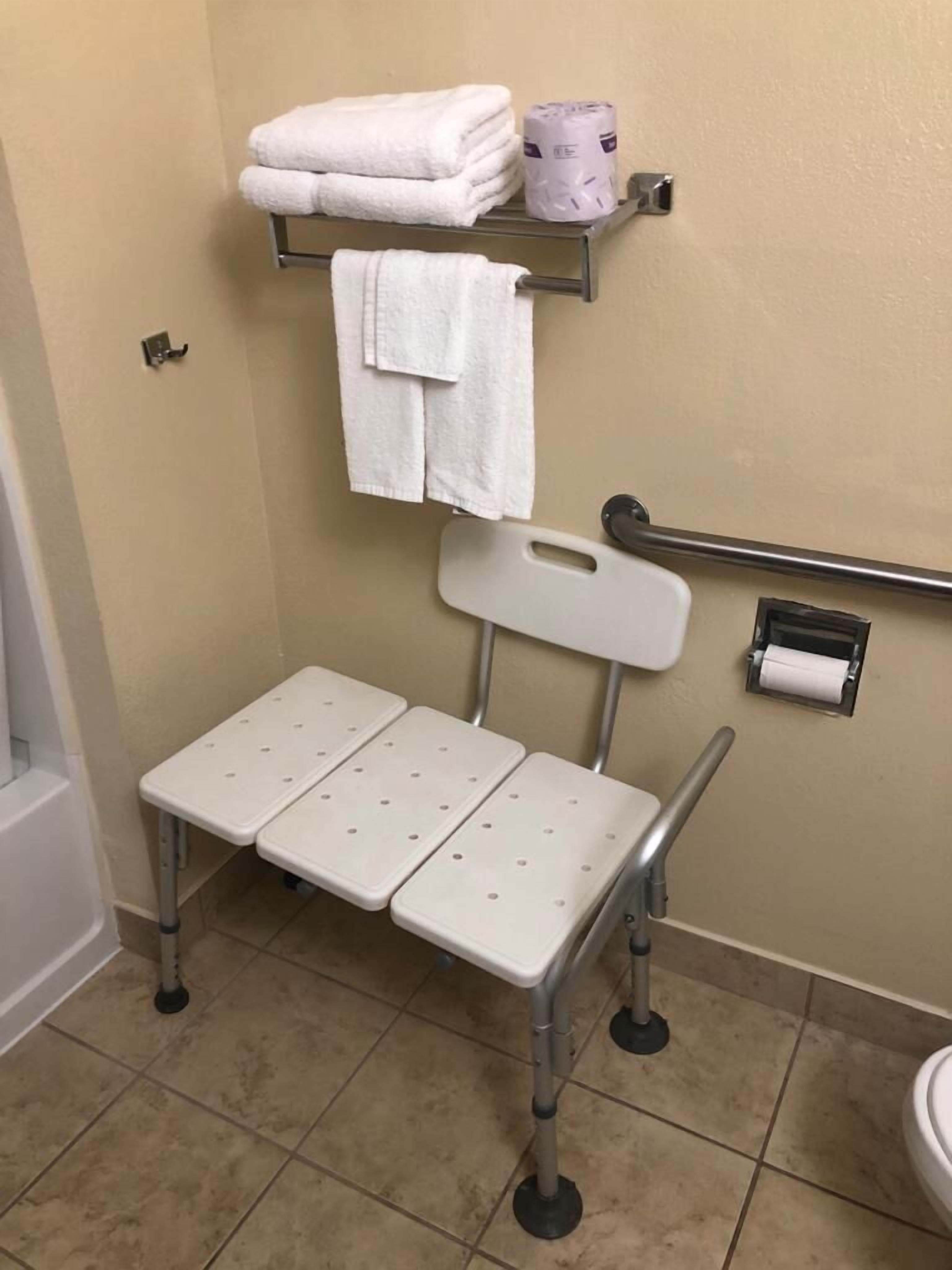A bathroom with a white toilet, a sink, a mirror, a shelf with towels, and a grab bar.