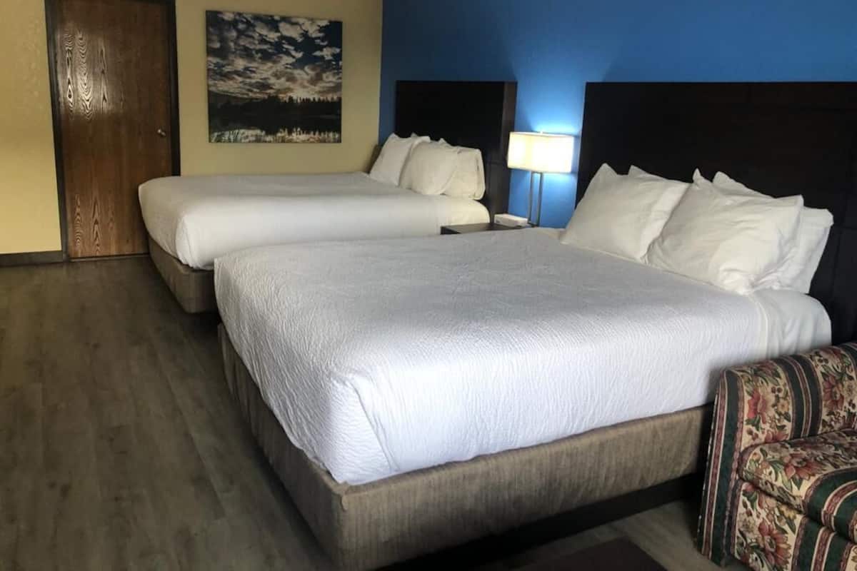 A hotel room with two beds, a wooden floor, a blue accent wall, and a door.
