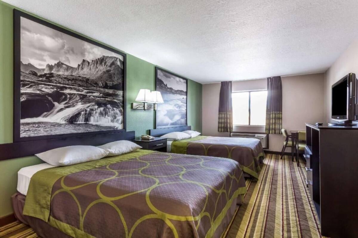 Een hotelkamer met twee bedden, een bureau met een televisie, een groot fotokader met een waterval en een raam met gordijnen.
