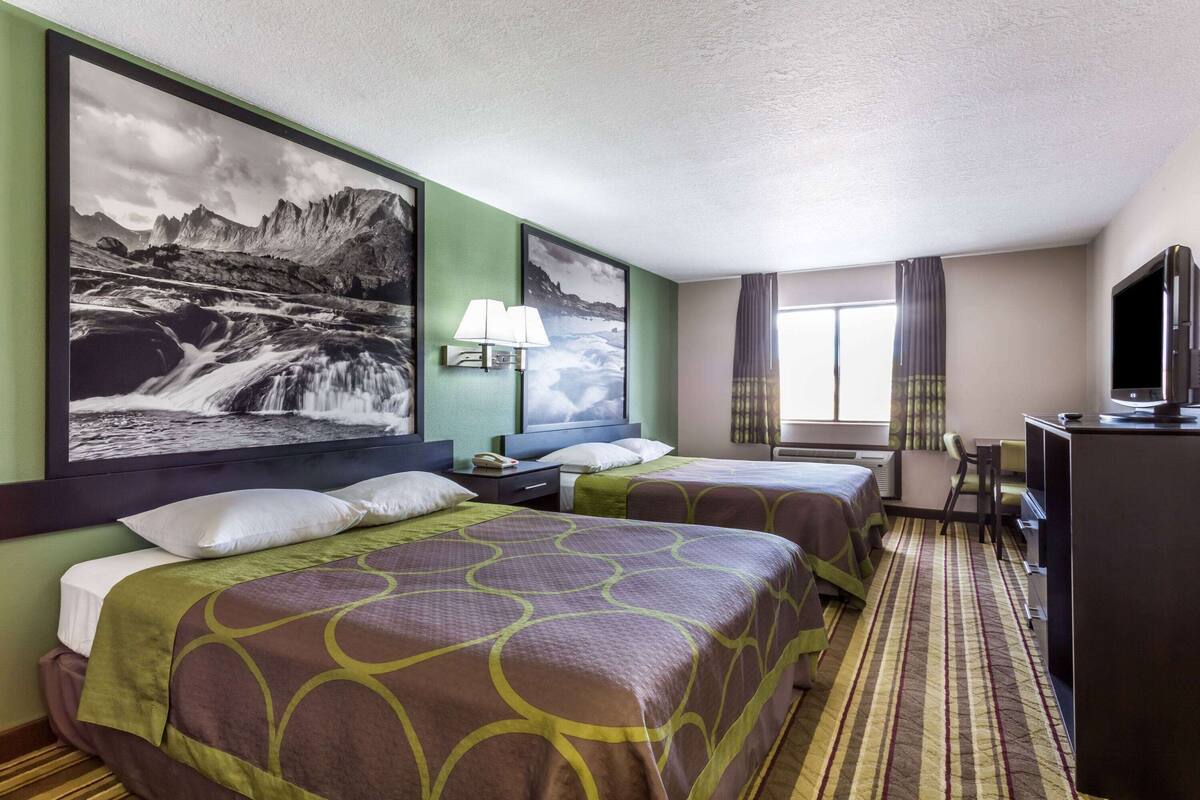 Een hotelkamer met twee bedden, een bureau, een televisie en een groot landschap op de muur.