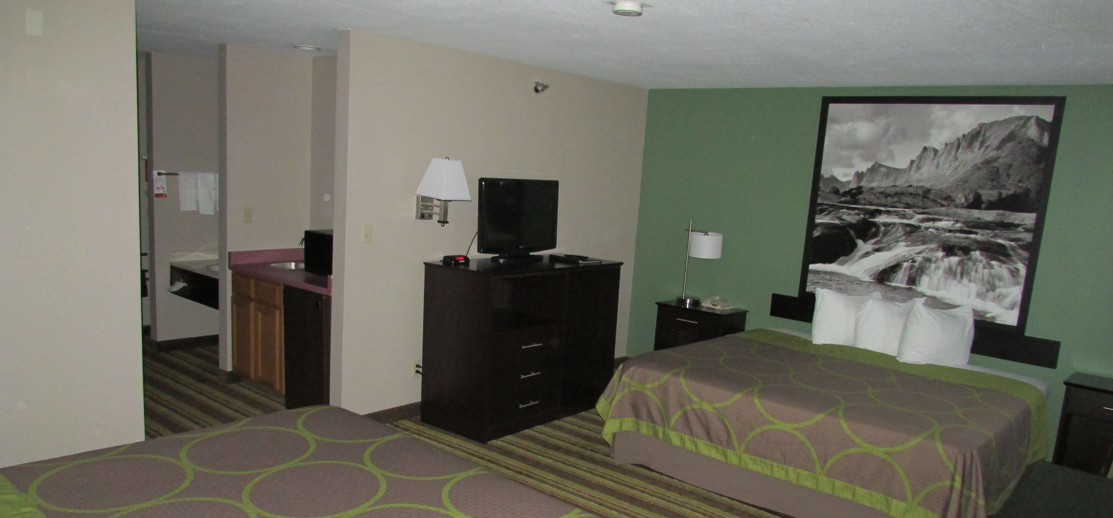 Habitación de hotel con cama, escritorio, silla, espejo, cómoda y televisor montado en la pared.