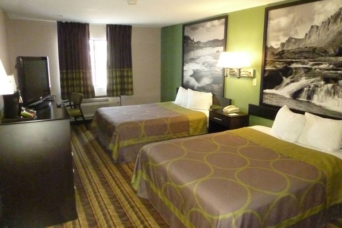 Een hotelkamer met twee bedden, een bureau, een televisie en een groot landschap op de muur.
