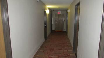 Un pasillo de hotel con pisos alfombrados, puertas a ambos lados y una señal de salida al final.