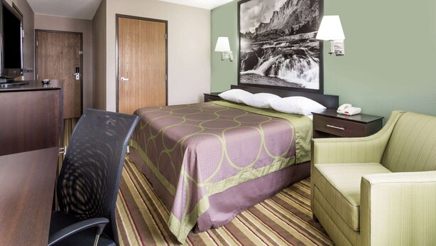 Een hotelkamer met een bed, een bureau, een stoel, een nachtkastje en een wandlamp.
