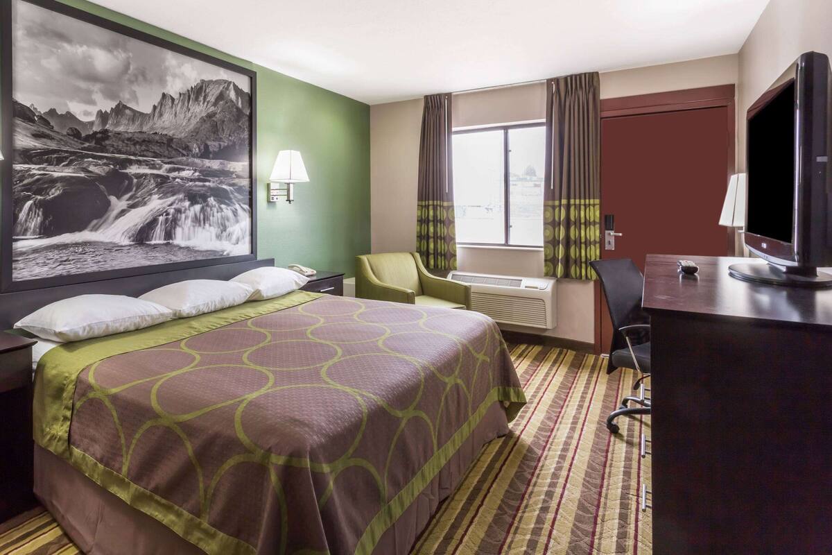 Een hotelkamer met een groot bed, een bureau met een televisie, een stoel en een raam met gordijnen.