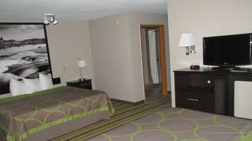 A hotel room with a bed, a desk with a television, a lamp, and a picture of a river.